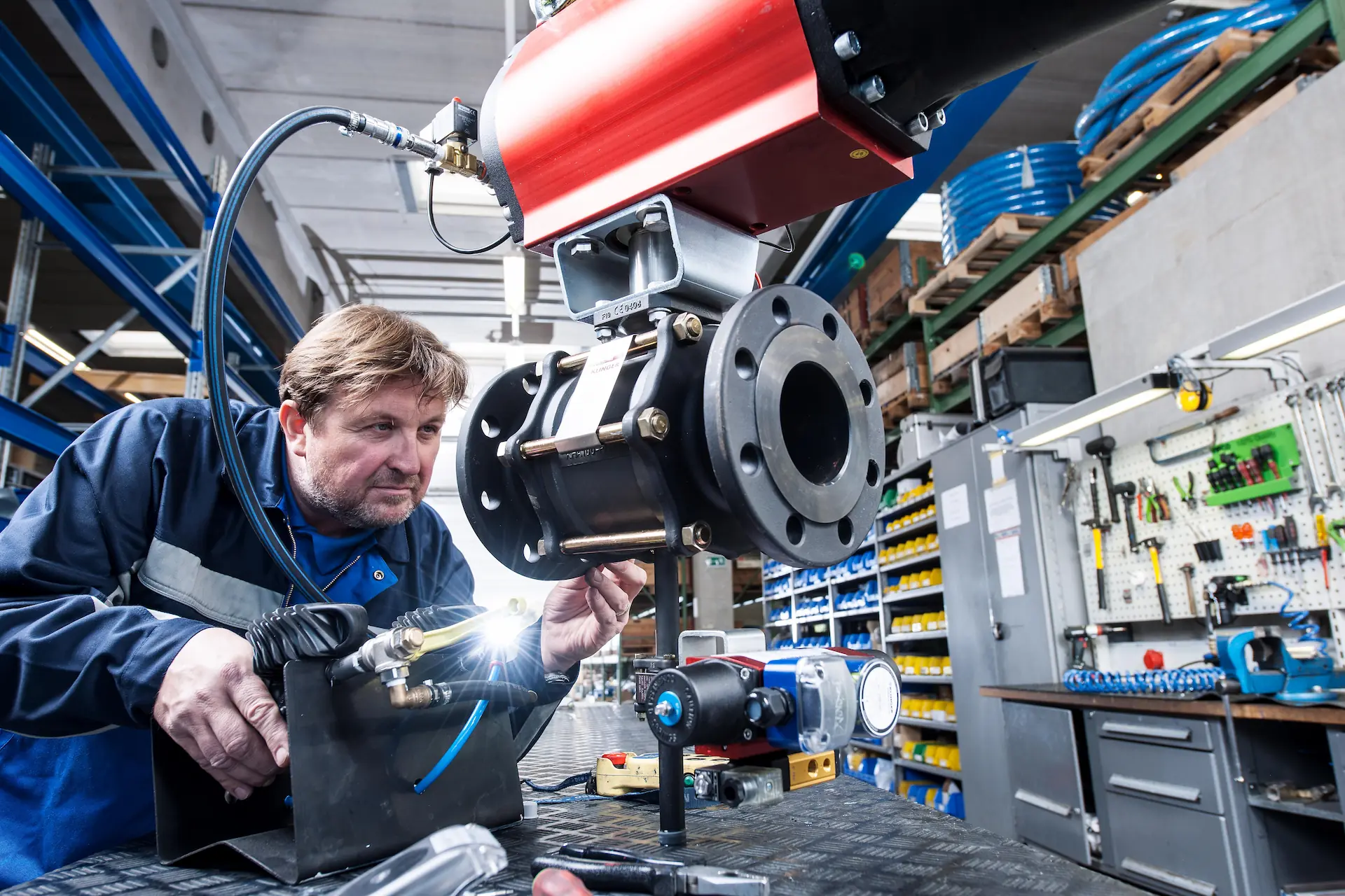 KLINGER employee working on valve in workshop with tools on wall behind him